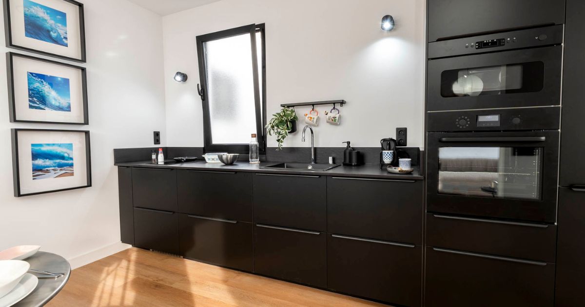 Cocina negra con pared blanca ventana y cuadros a los lados en Gran Canaria