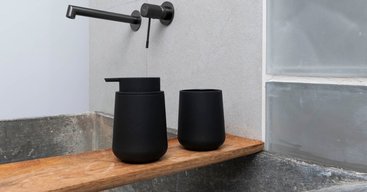 Dispensador de jabon y vaso negro sobre tabla de madera en una pequeña reforma