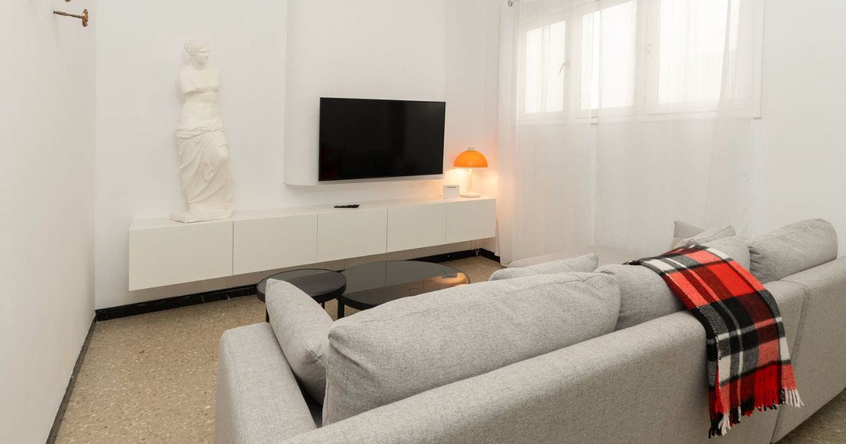 Salón reformado con sofá gris, mueble blanco y televisión empotrada en Gran Canaria